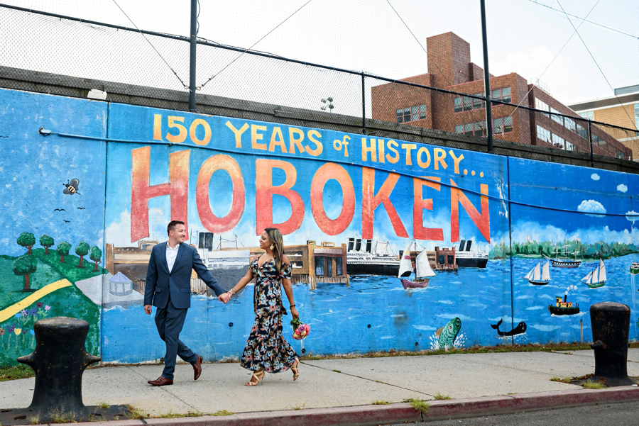 An Engaged couple walk in front of a Hoboken mural for thier engagement session.